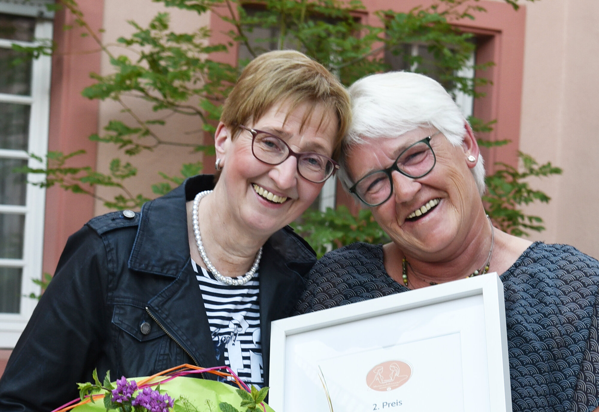Zwei Frauen mit Urkunde und Blumenstrauß