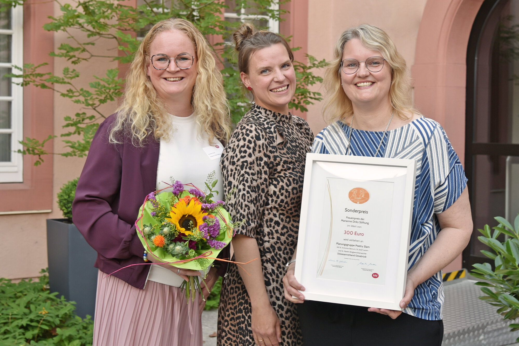 Drei Frauen mit Blumenstrauß und Urkunde